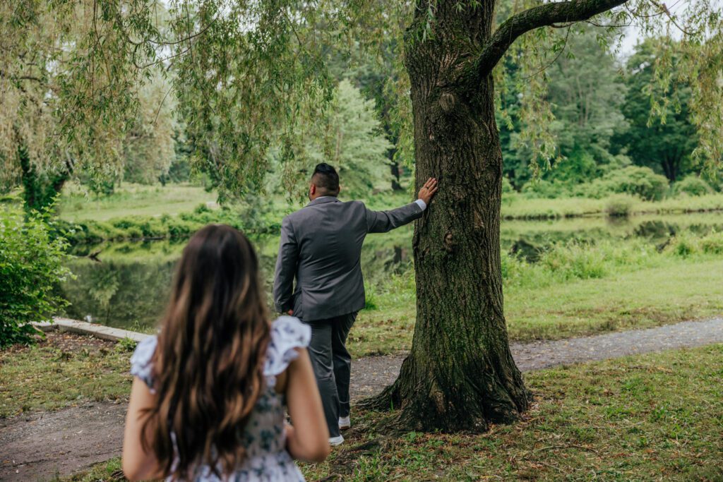 Groom leaning on tree as his daughter approaches for first look at whimsical wedding at Bird Park in Walpole, Massachusetts.