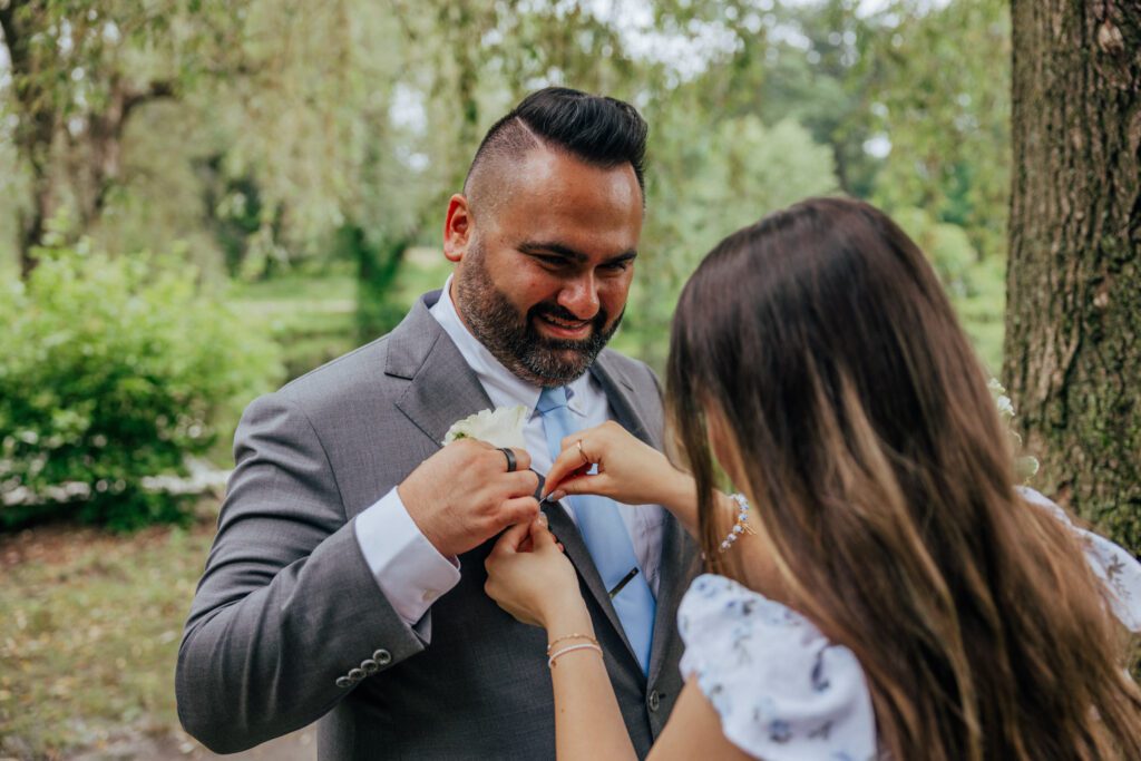 Daughter helps groom put on boutonniere at Bird Park in Walpole, Massachusetts.