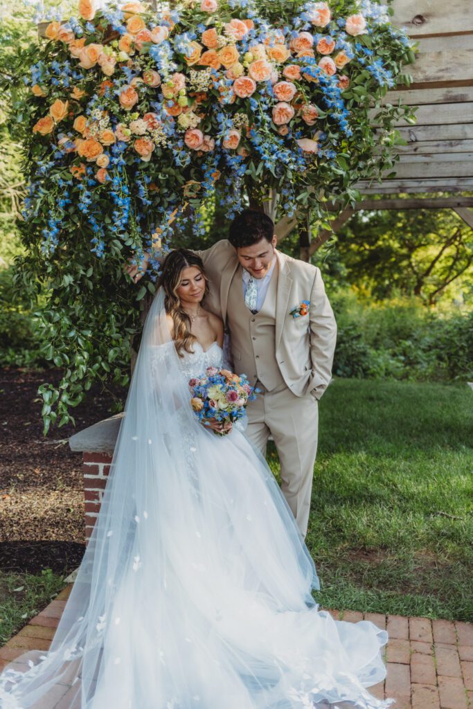 Bride and groom standing underneath floral arch at a summer fairytale wedding at Peirce Farm Estate in Topsfield, Massachusetts.