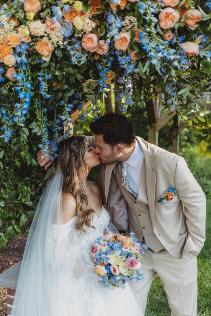 Bride and groom romantically kissing under flower arch way outside at Peirce Farm Estate in Topsfield, Massachusetts.