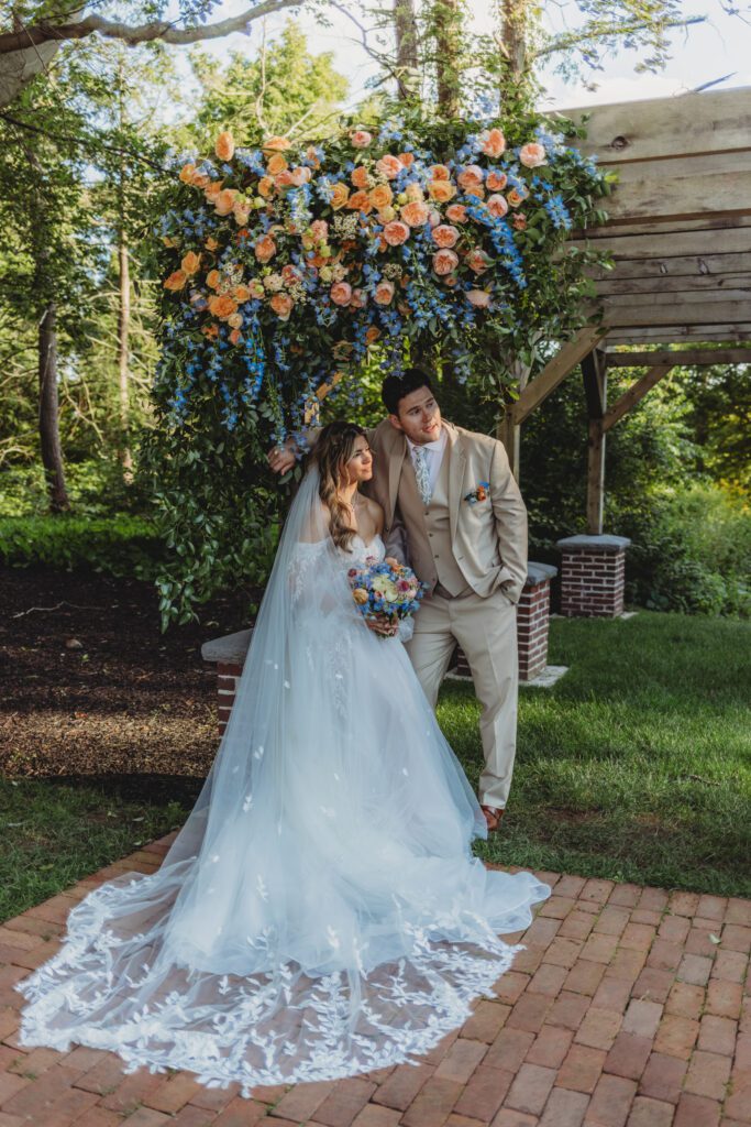 Bride and groom thoughtfully looking into the distance as they stand under a flower archway at Peirce Farm Estate in Topsfield, Massachusetts.