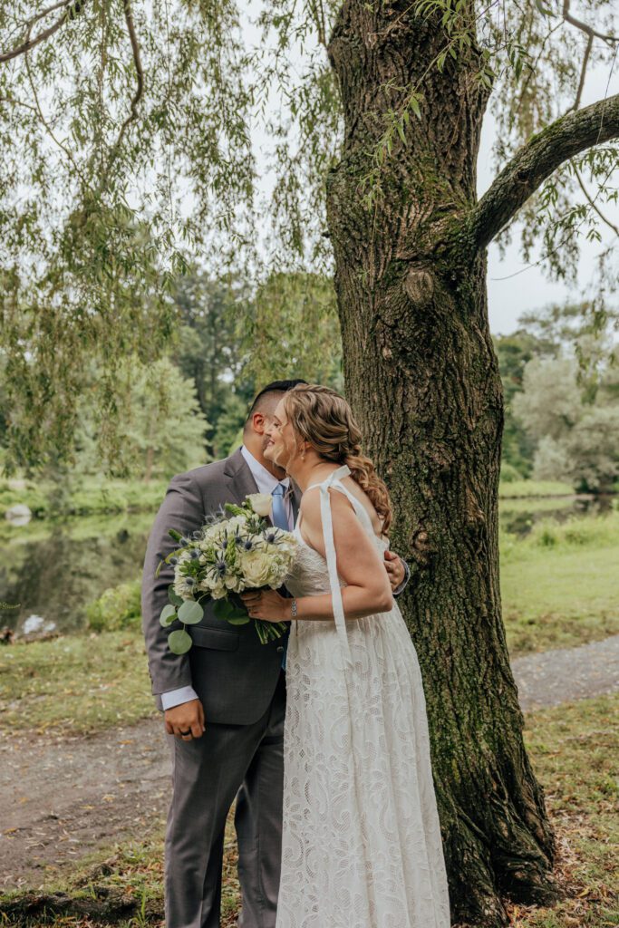 Groom kisses bride on the cheek during first look at Bird Park in Walpole, Massachusetts.