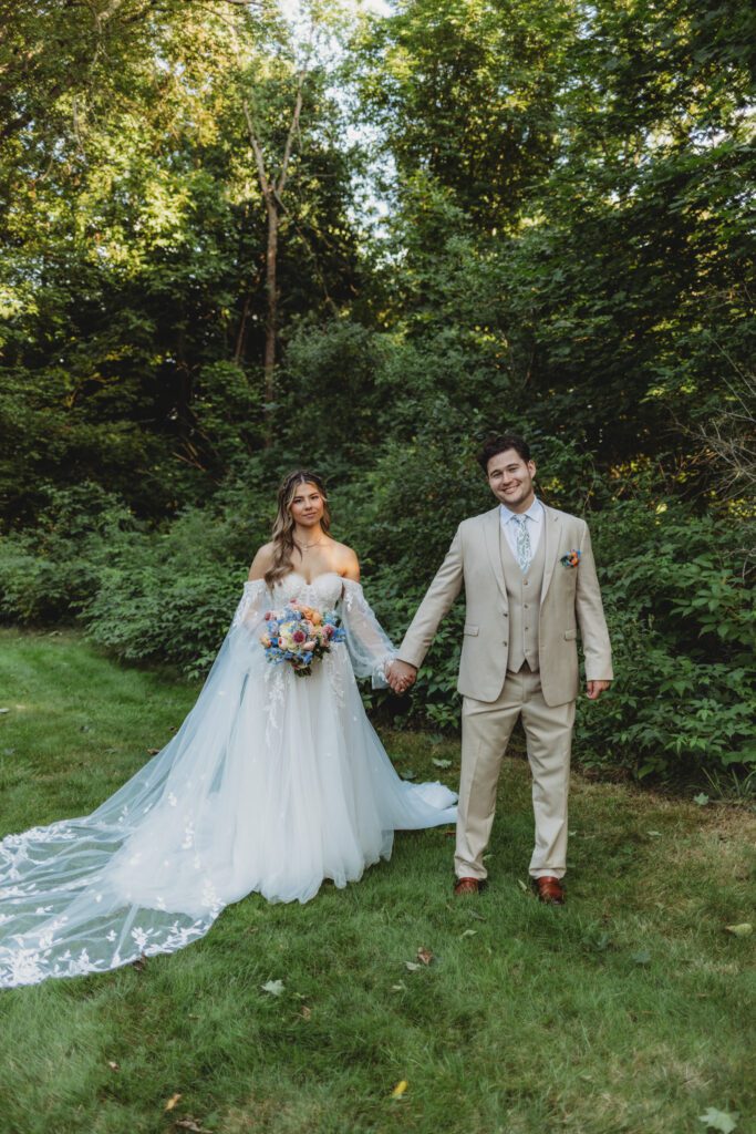 A bride and groom romantically holding hands and smiling outside surrounded by greenery at Peirce Farm Estate in Topsfield, Massachusetts.