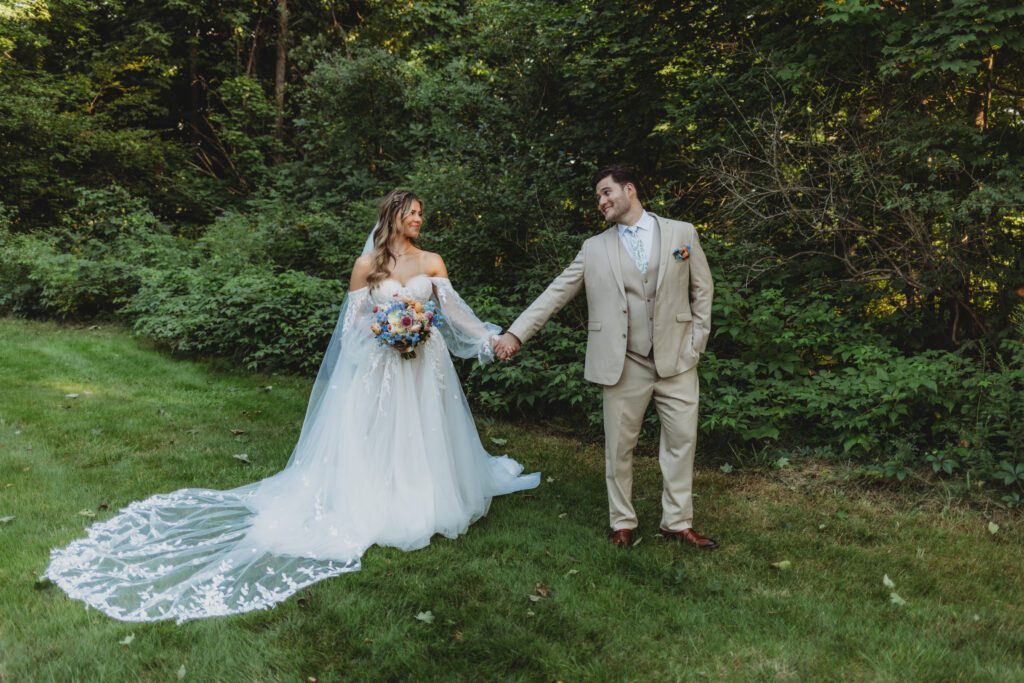 Bride and groom romantically holding hands and looking at each other smiling surrounded by greenery at Peirce Farm Estate in Topsfield, Massachusetts.