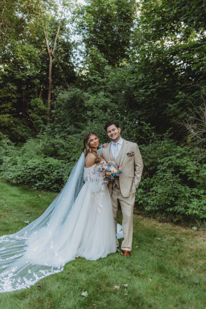 Bride and groom romantically smiling in front of greenery at whimsical wedding at Peirce Farm Estate in Topsfield, Massachusetts.