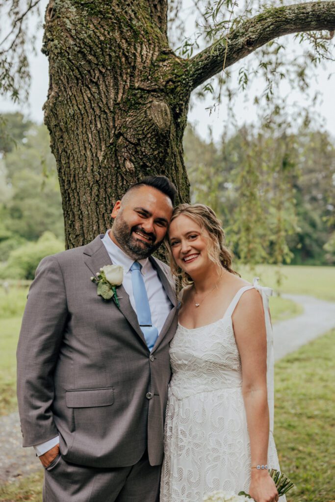Bride and groom smiling surrounded by greenery during their summer wedding at Bird Park in Walpole, Massachusetts.