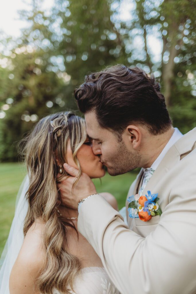 Bride and groom kiss at their romantic summer wedding surrounded by greenery at Peirce Farm Estate in Topsfield, Massachusetts.