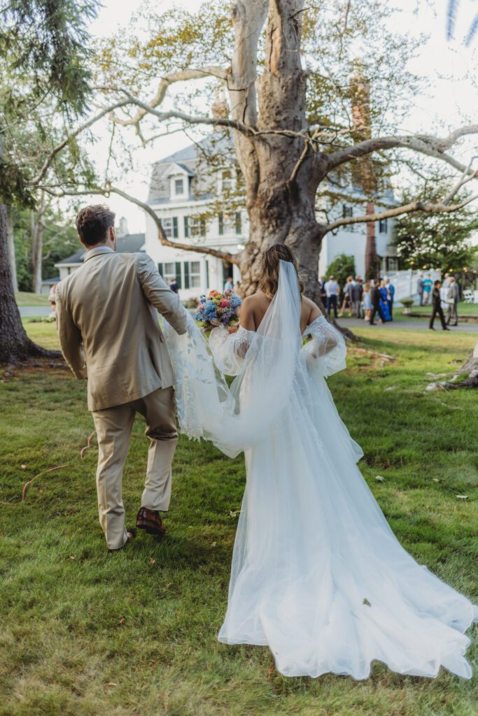 Groom romantically carries brides veil as they walk away at Peirce Farm Estate in Topsfield, Massachusetts.