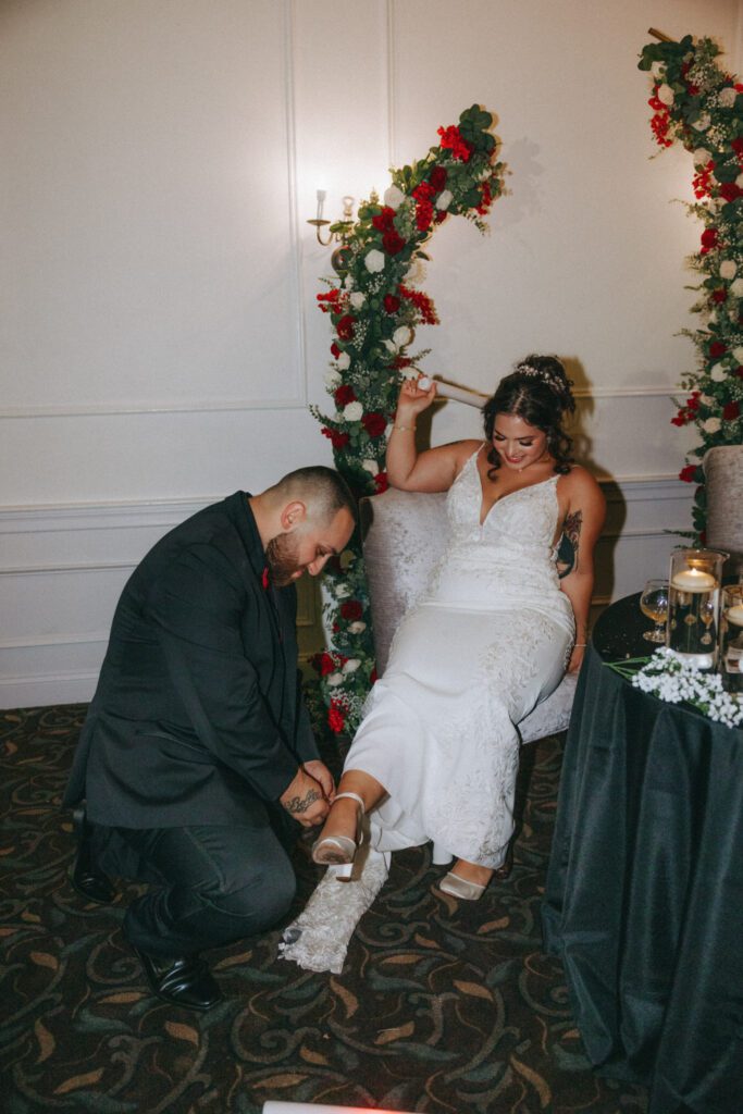 Groom romantically taking off a brides shoe during wedding reception at Black Swan Country Club in Georgetown, Massachusetts.