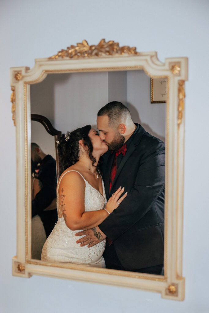 Bride and groom romantically kissing in bridal suite in mirror reflection at Black Swan Country Club in Georgetown, Massachusetts.