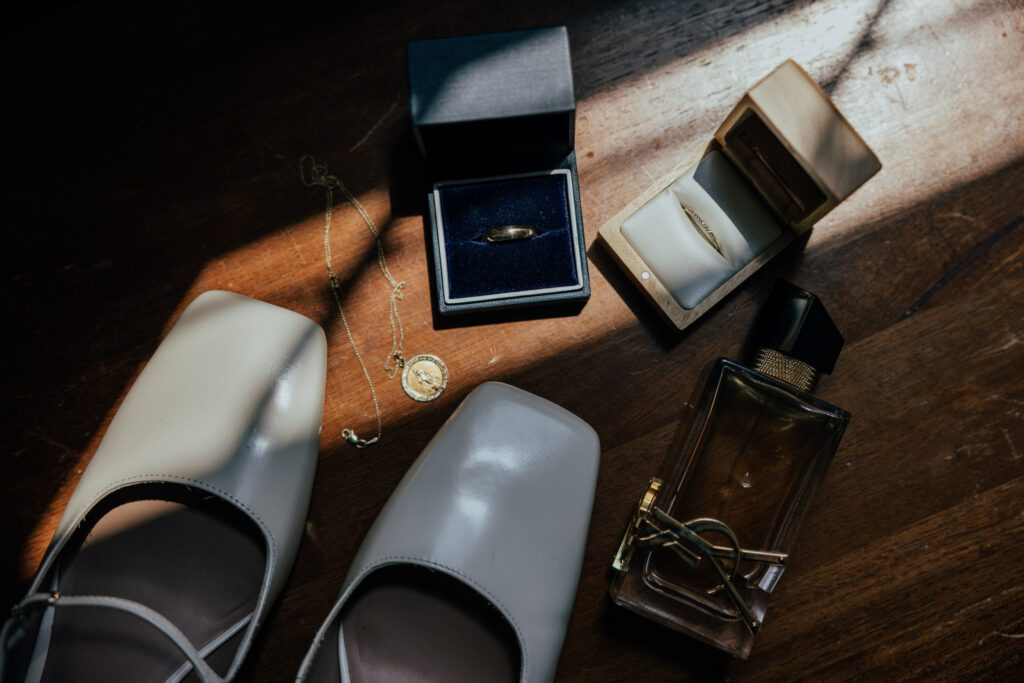Rings, wedding shoes, necklace on a wooden table with sunlight shining on it in Massachusetts.
