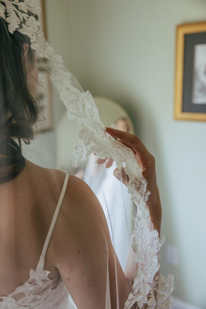 Bride getting ready and touching the lace on her veil at wedding in Massachusetts.