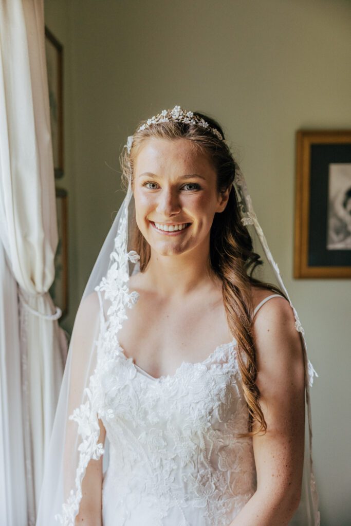 Bride smiling in front of a window during a summer wedding in Massachusetts.