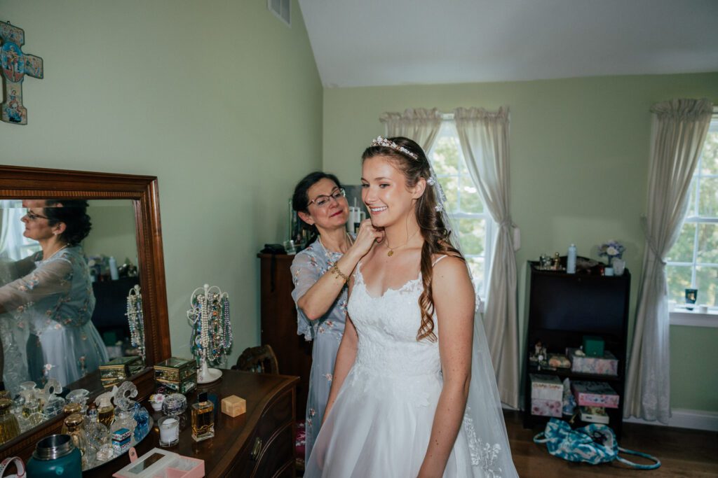 Mother of the bride puts necklace on bride as she is getting ready for Massachusetts wedding.