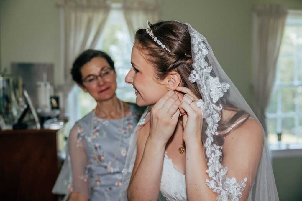 Bride is putting on earrings as she is getting ready for romantic summer wedding in Massachusetts.