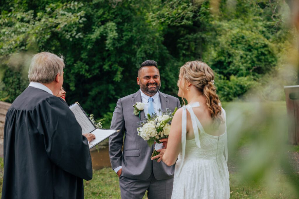 Groom smiling at bride during summer elopement ceremony at Bird Park in Walpole, Massachusetts.