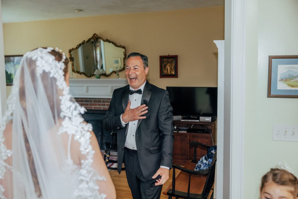 Father of the bride laughing and smiling during first look with his hand on his heart during Massachusetts wedding.