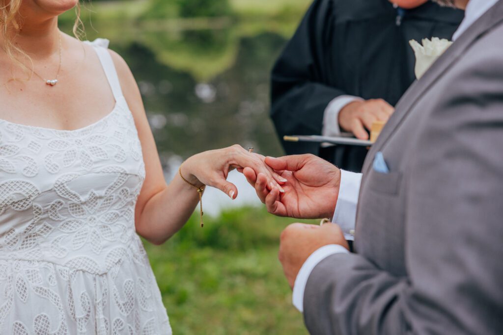 Groom putting ring on bride hand during outdoor wedding ceremony at Bird Park in Walpole, Massachusetts.