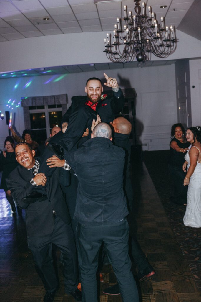 Groomsmen lifting groom in the air during the reception as they all laugh at Black Swan Country Club in Georgetown, Massachusetts.