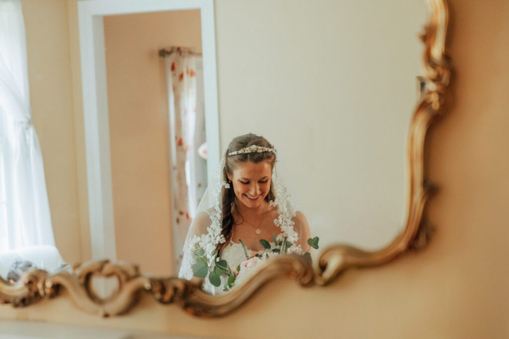 Bride looking down at her bouquet and smiles in the reflection of a gold mirror in Massachusetts.