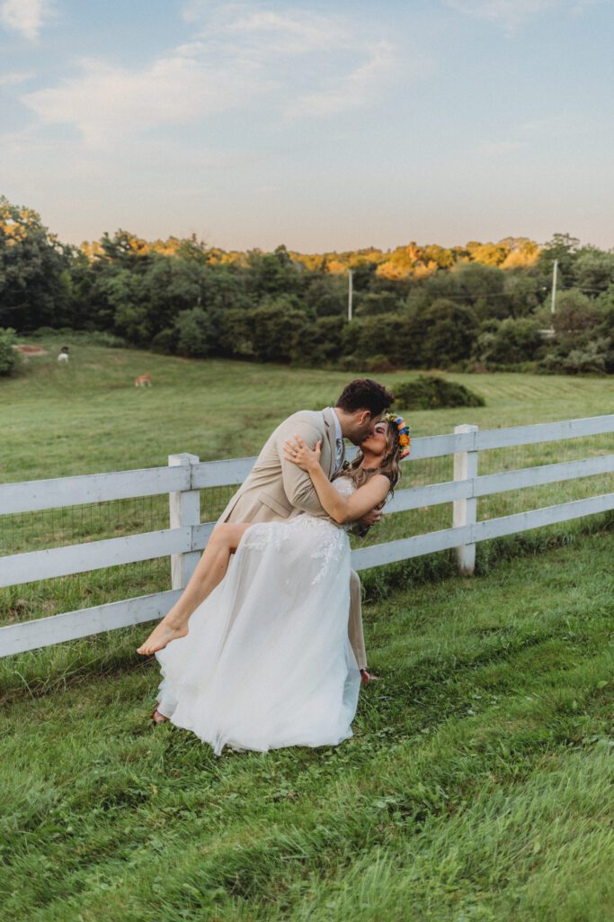 Groom dipping bride in front of white fence during a romantic sunset at Peirce Farm Estate in Topsfield, Massachusetts.