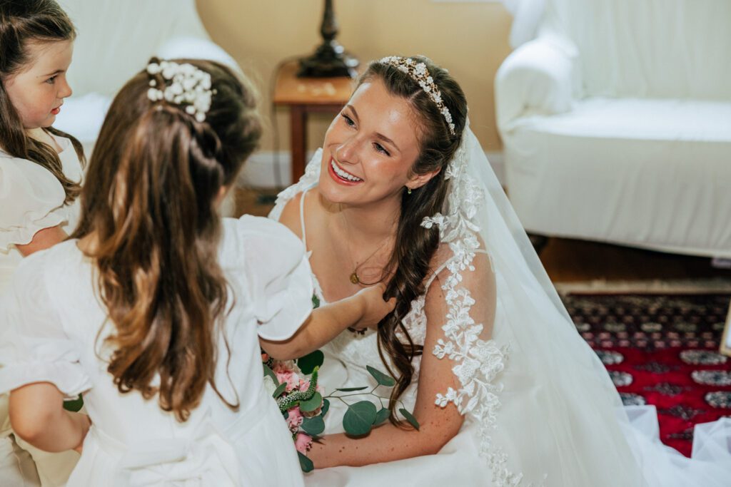 Bride is smiling at flower girls as the girl plays with brides hair for romantic summer wedding in Massachusetts.