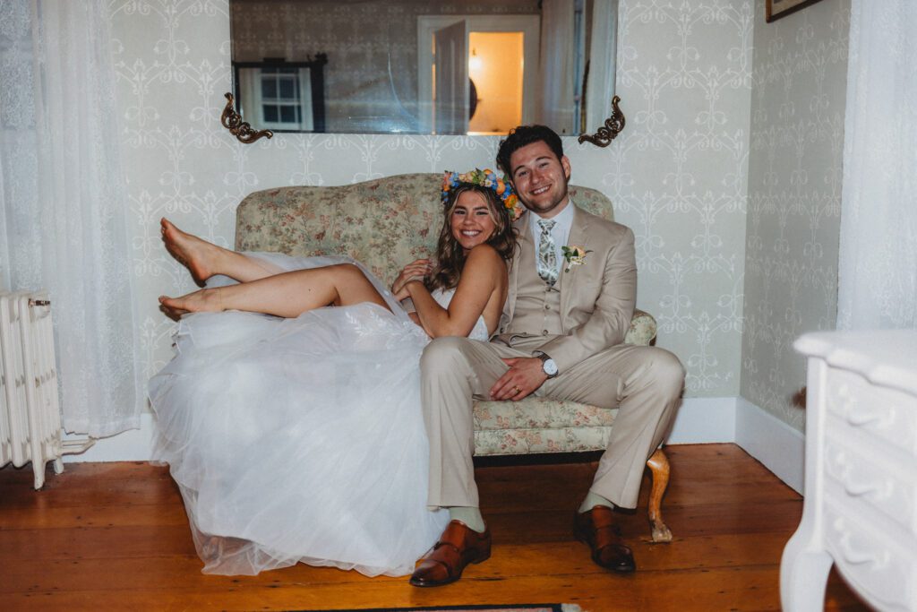 Bride and groom sitting on couch smiling together in the bridal suite at Peirce Farm Estate in Topsfield, Massachusetts.