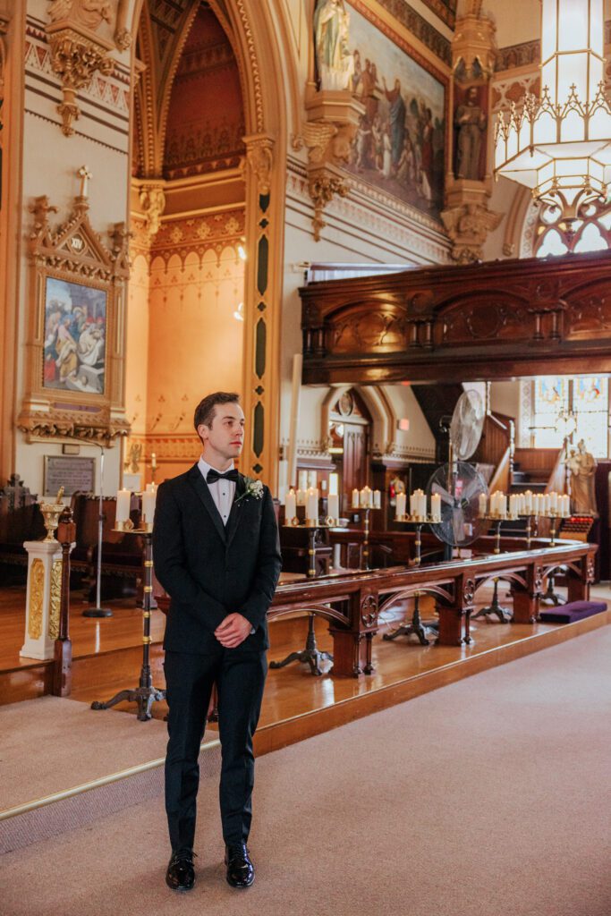 Groom standing as bride walks towards him in summer wedding ceremony at Quinet Saint John Garden of Our Lady in Massachusetts.