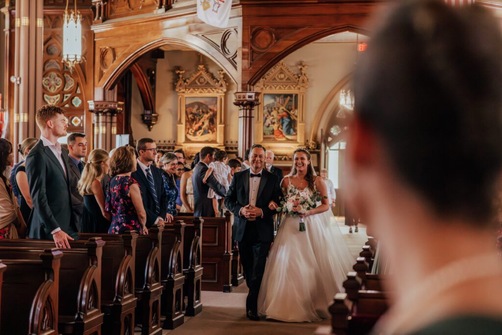 Bride smiling with her father walking down the aisle at Quinet Saint John Garden of Our Lady in Massachusetts.