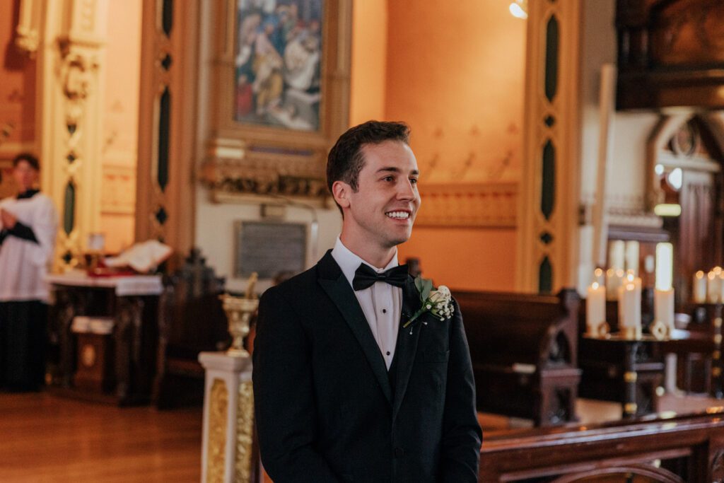 Groom smiling reaction to seeing bride walk dow the aisle at Quinet Saint John Garden of Our Lady in Massachusetts.