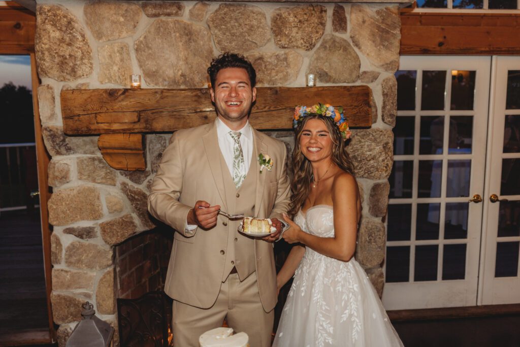 Bride and groom smile as they hold wedding cake at romantic barn reception at Peirce Farm Estate in Topsfield, Massachusetts.
