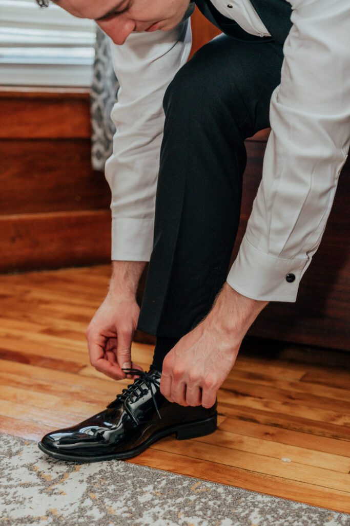 Groom tying his shoe as he gets ready for Massachusetts wedding.