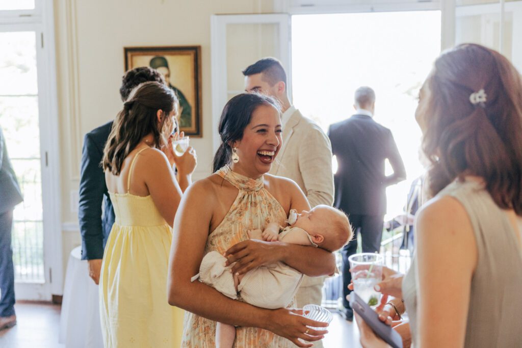 Guest laughing while holding a baby during cocktail hour in Massachusetts.