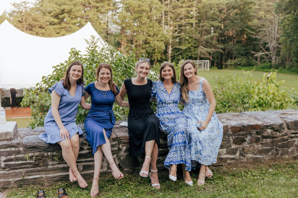 Guests sitting on stone wall smiling during cocktail hour in Massachusetts.