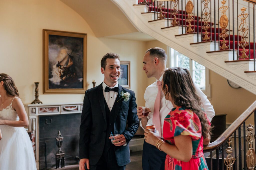 Groom smiling and talking to guest during wedding cocktail hour in Massachusetts.