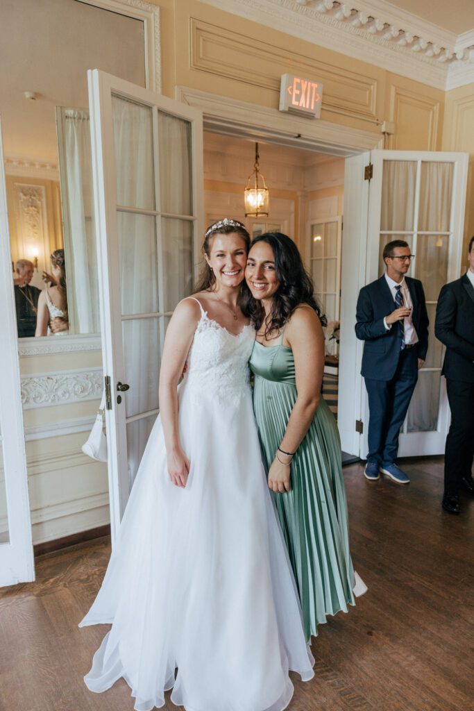 Bride and guest smiling indoors in Massachusetts.