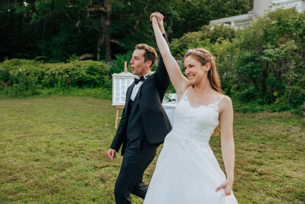 Bride and groom hands in the air as they walk into reception in Massachusetts.