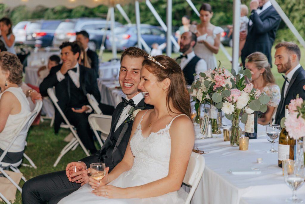 Groom smiling at the bride as she laughs at wedding reception speech in Massachusetts.