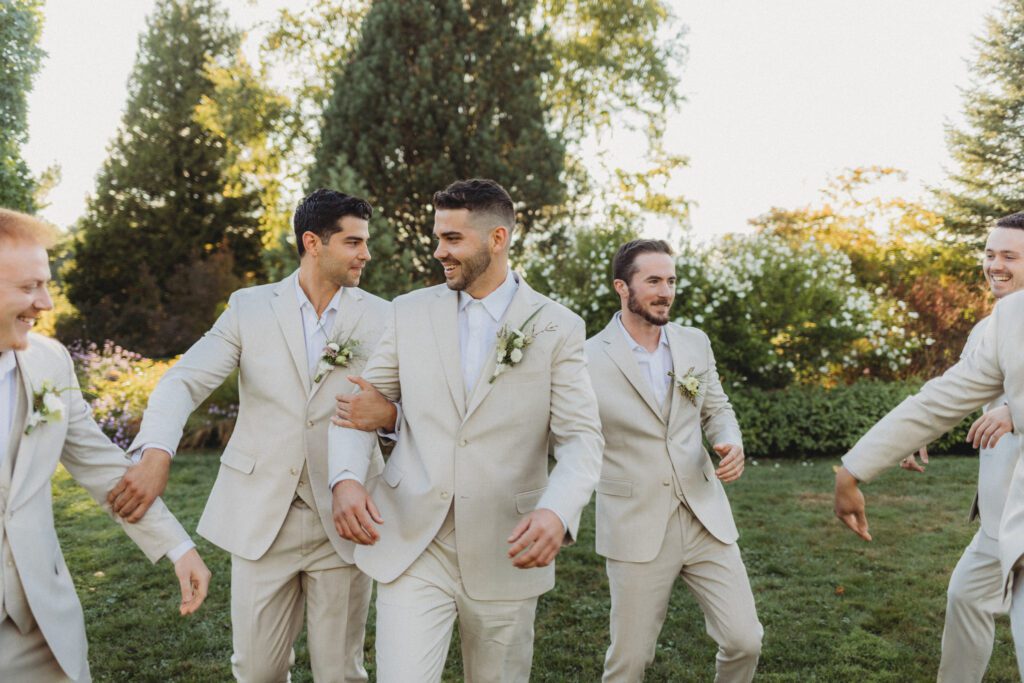 Groom and groomsmen walking and playfully pushing each other around in a garden at Tower Hill in Boylston, Massachusetts.