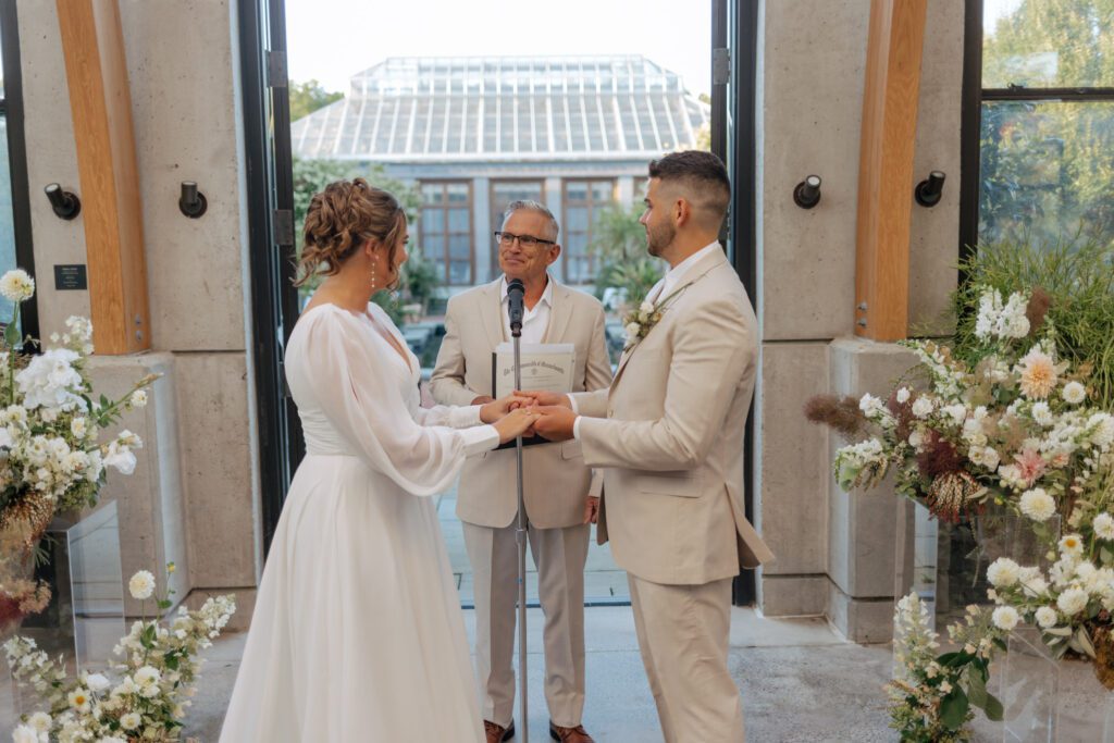Bride and groom hold hands during greenhouse wedding ceremony at Tower Hill in Boylston, Massachusetts.