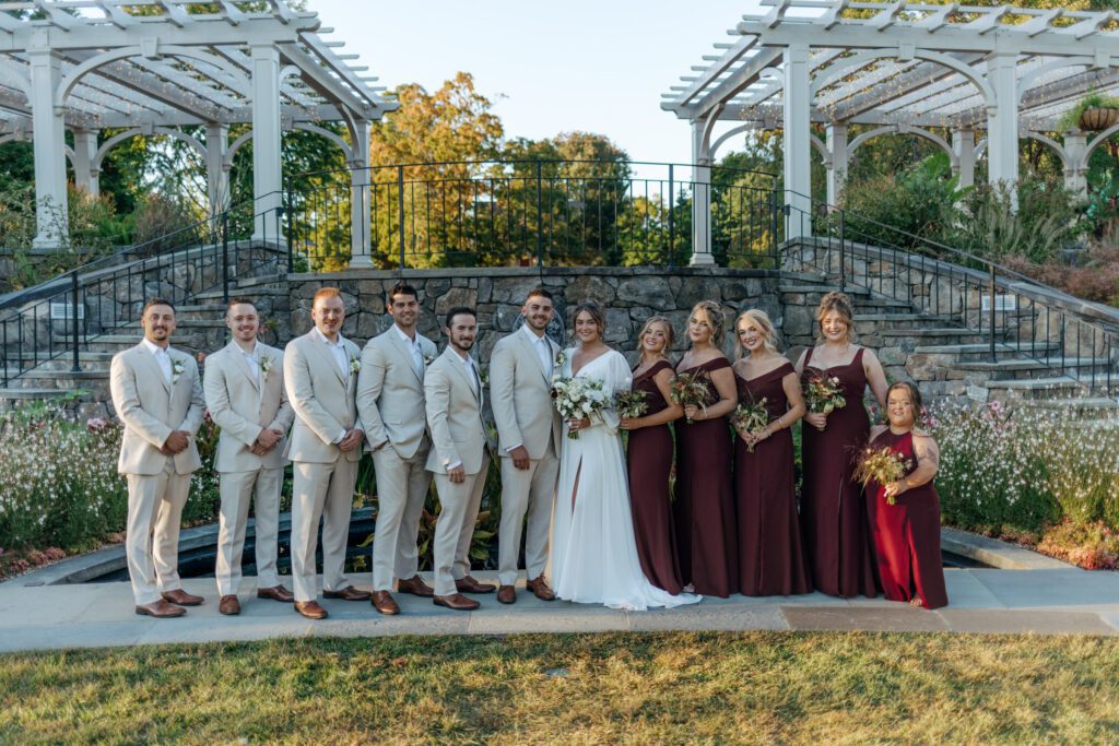 Bridal party standing together in a line smiling in front of stone stair case at Tower Hill in Boylston, Massachusetts.