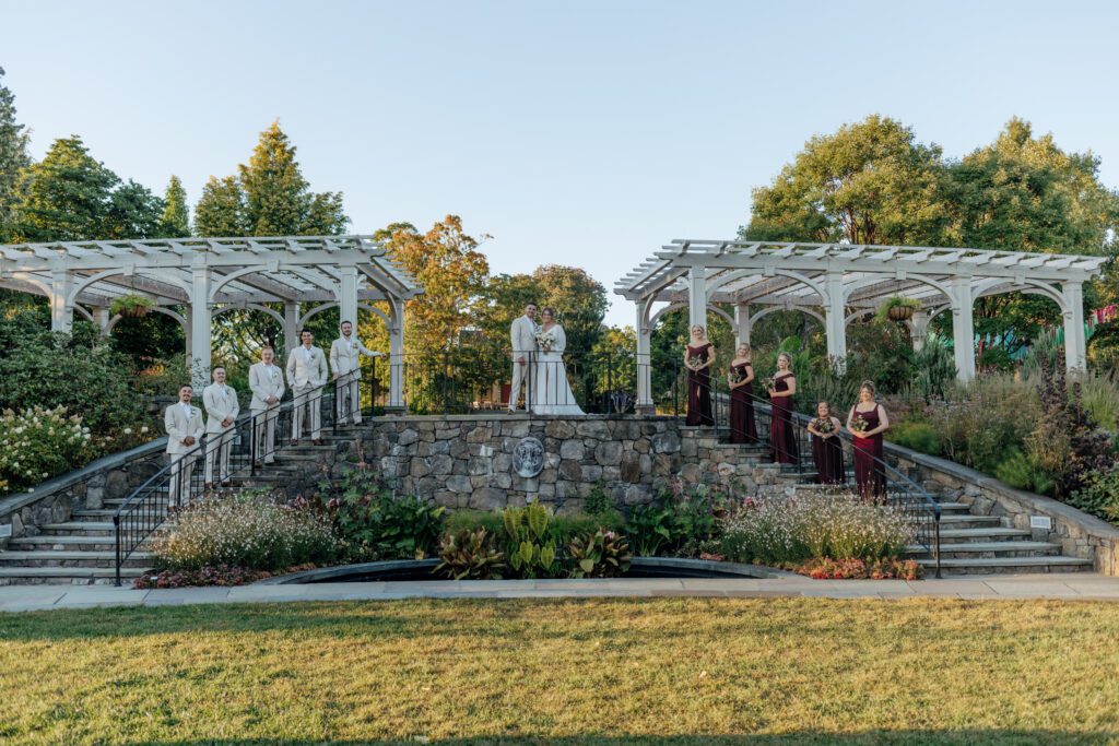Bridal party standing on elegant stone stair case at Tower Hill in Boylston, Massachusetts smiling.