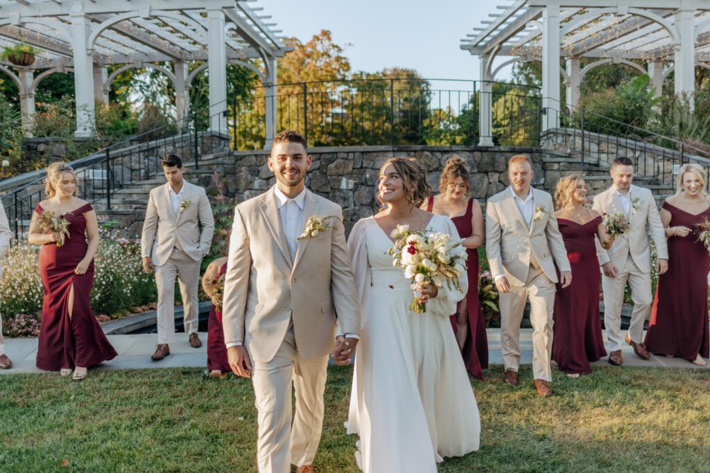 Bride and groom walking with bridal party smiling behind them in front of stone stairs at Tower Hill in Boylston, Massachusetts.
