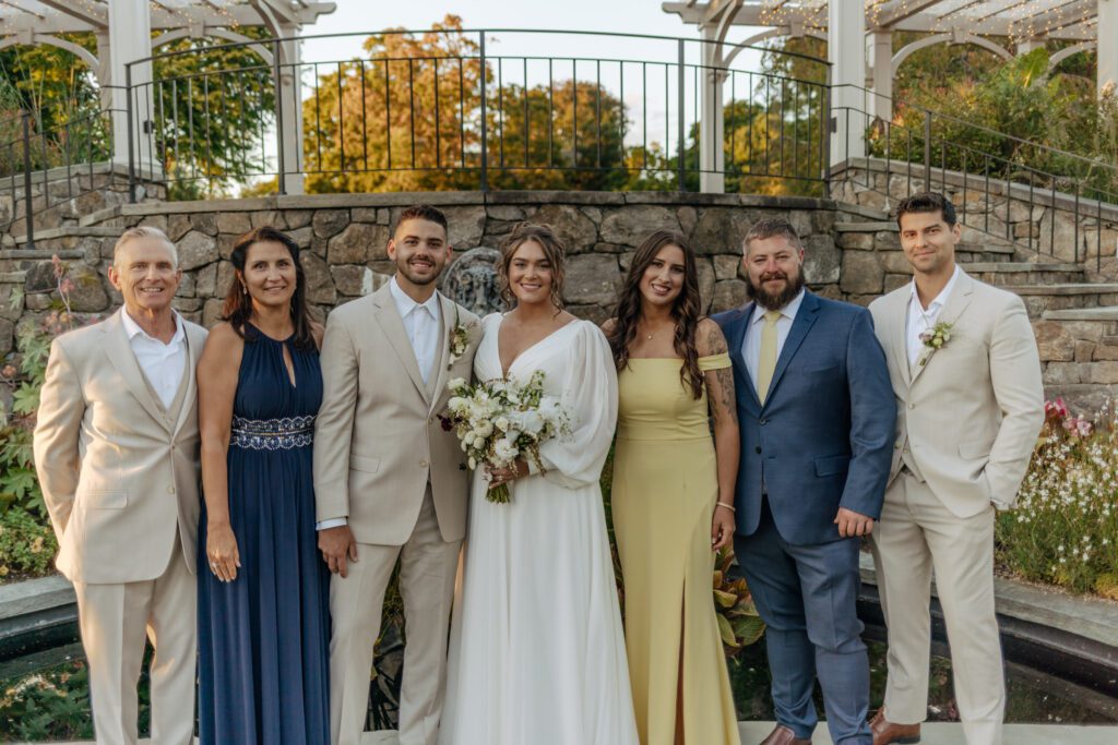 Bride and groom smile with family in from of stone stairs at Tower Hill in Boylston, Massachusetts.