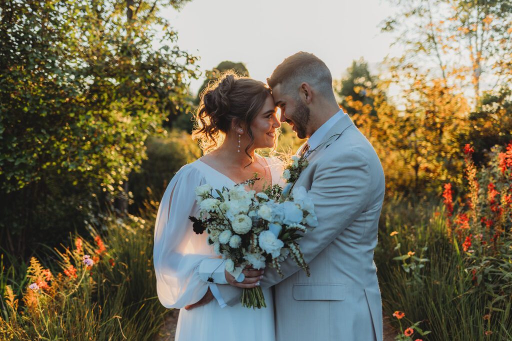 Bride and groom have either heads together and are smiling with the sun shining behind them romantically New England Botanical Garden at Tower Hill in Boylston, Massachusetts.