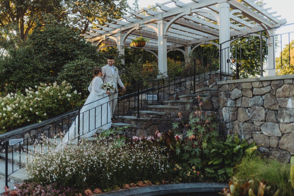 Bride and groom walking up romantic stone stairs as the groom looks back at a bride New England Botanical Garden at Tower Hill in Boylston, Massachusetts.