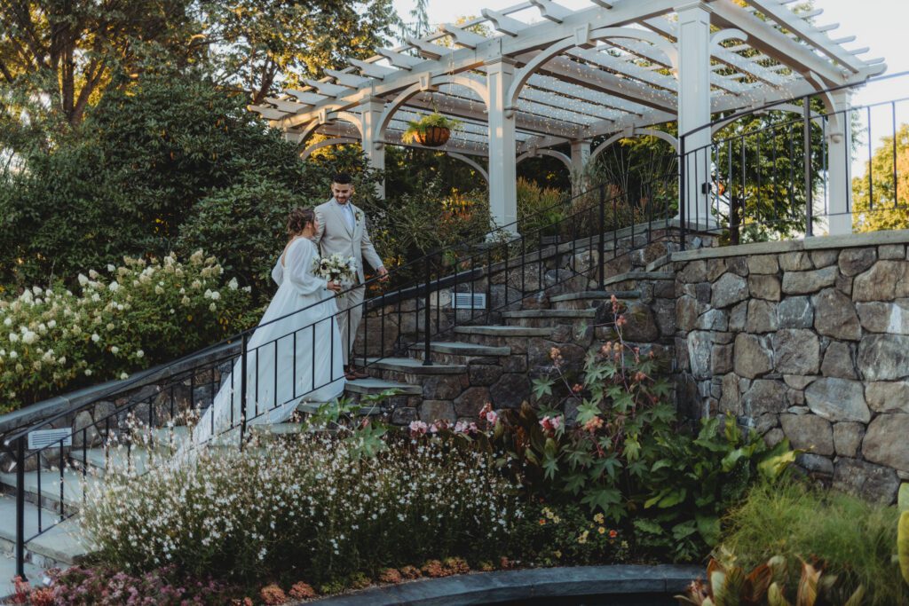 Bride and groom romantically walk up stone stairs holding hands and looking at each other at Tower Hill in Boylston, Massachusetts.