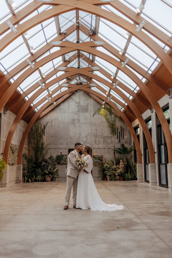 Bride and groom romantically kiss in greenhouse at Tower Hill in Boylston, Massachusetts.