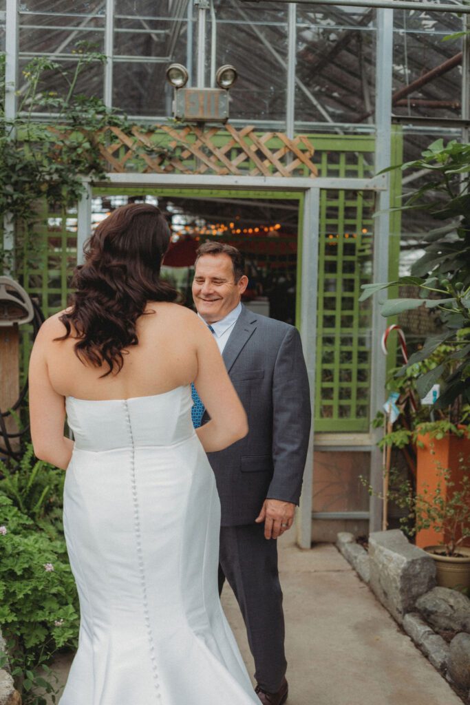 Father of the bride smiling during first look with the bride in greenhouse at Roger Williams Botanical Garden Park in Providence, Rhode Island.