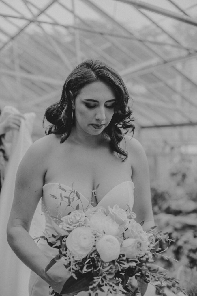 Bride looking down at flowers as her veil is put on her head in greenhouse at Roger Williams Botanical Garden Park in Providence, Rhode Island.
